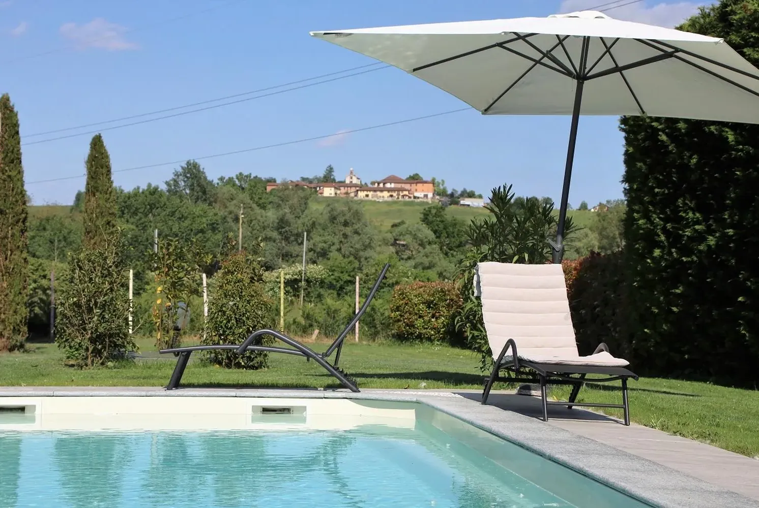 Sdraio e ombrellone a bordo piscina, con le colline