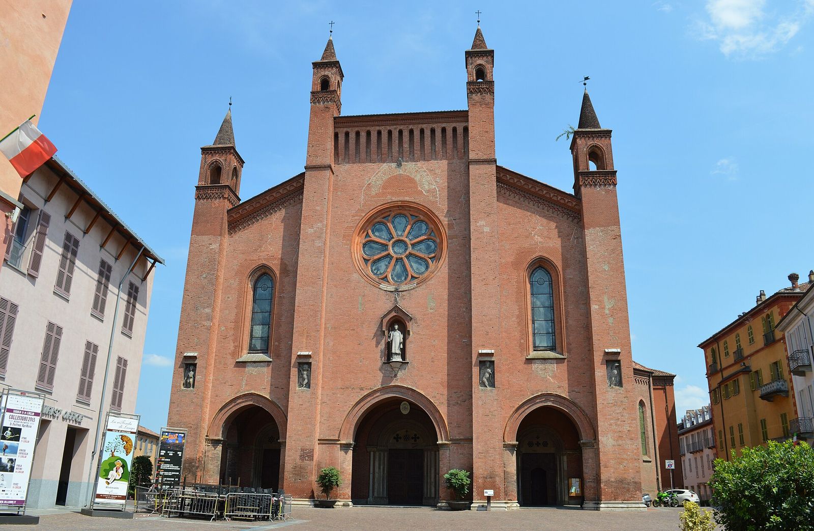 Facciata in mattoni rossi del Duomo di San Lorenzo ad Alba, con il rosone, i tre portali e i quattro pinnacoli, sotto un cielo azzurro