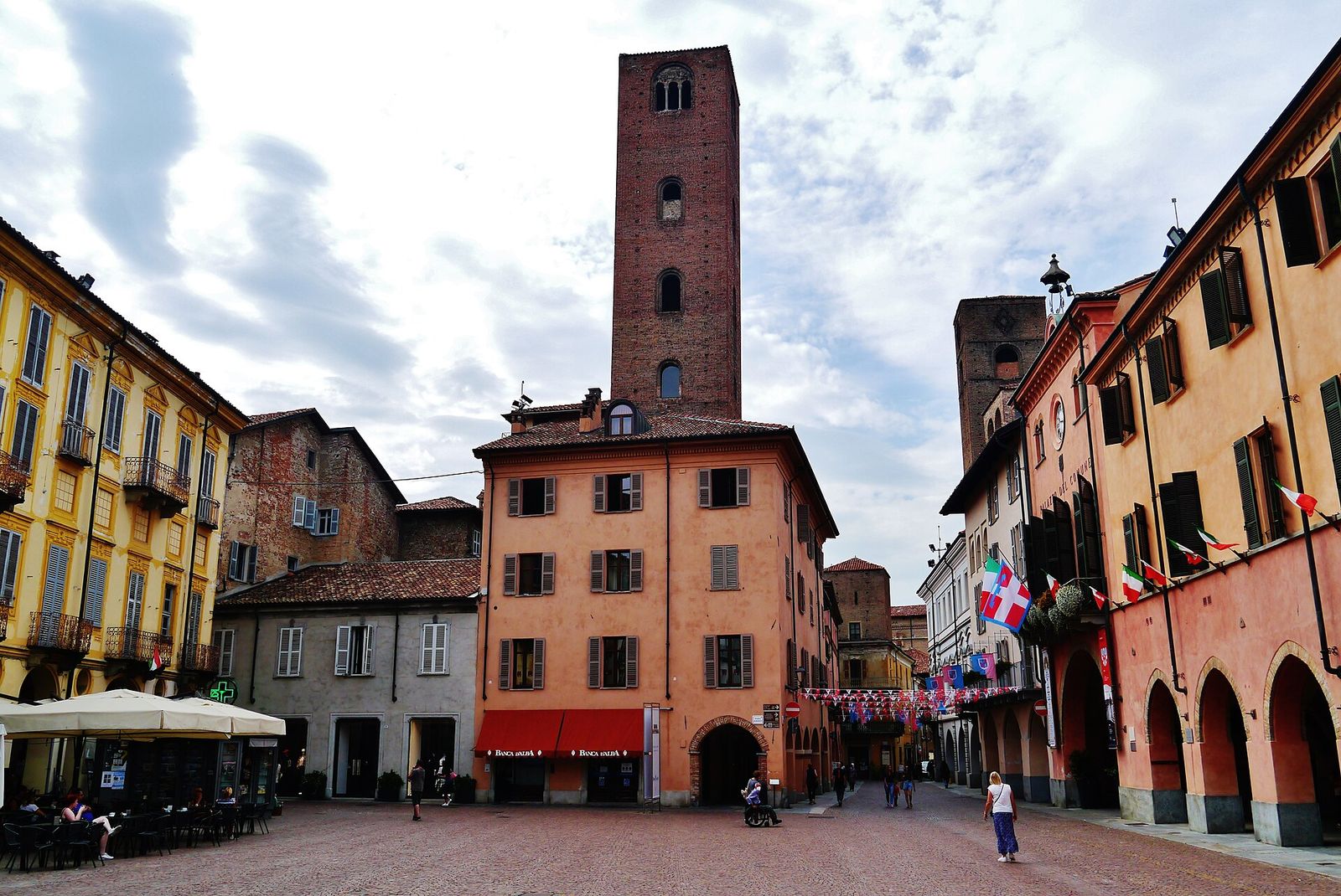 Piazza Risorgimento ad Alba con una torre medievale in mattoni al centro, palazzi colorati e portici ai lati
