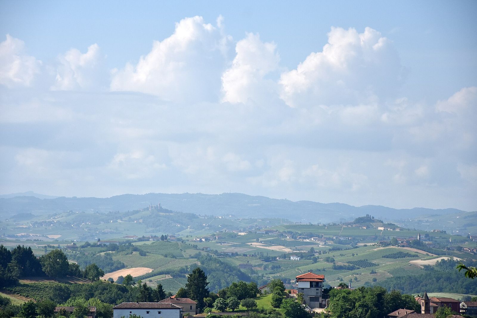 Panorama di colline del Monferrato con paesi, cascine e vigneti sparsi, visto da Mongardino sotto un cielo con grandi nuvole