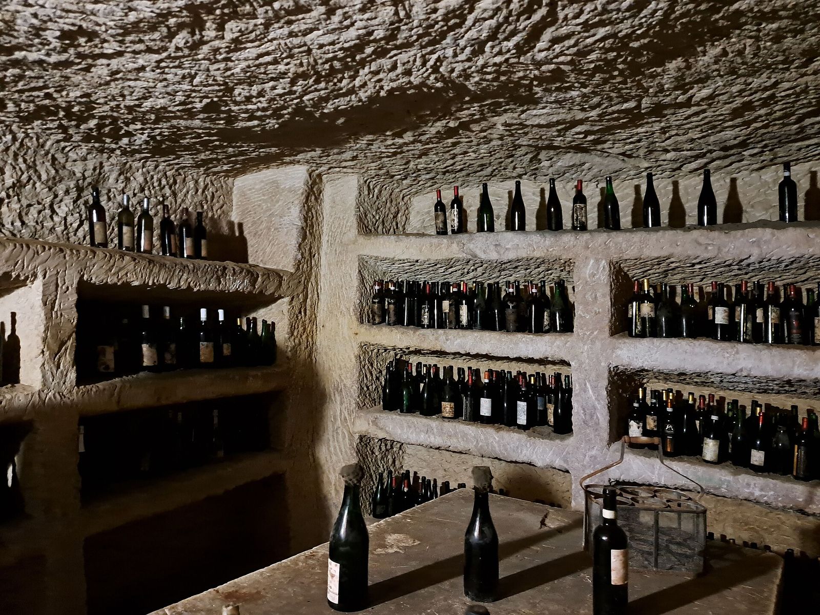 Interno di un infernot scavato nella pietra chiara, con ripiani ricavati nella roccia pieni di vecchie bottiglie di vino